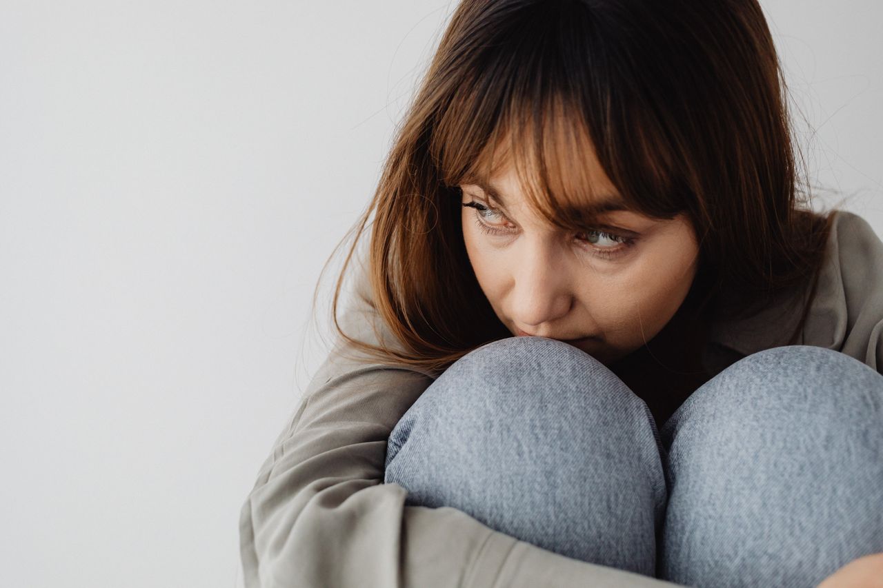 Close-up of a woman sitting pensively, deep in thought while hugging her knees.